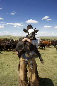 Man carrying calf while standing in field against sky