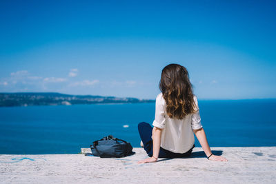 Rear view of woman sitting on shore against sea