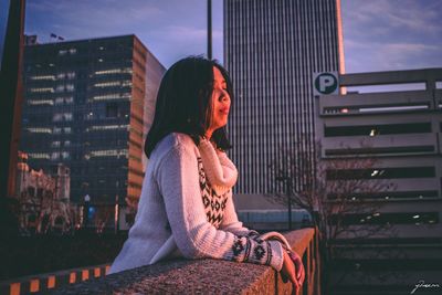 Full length of woman sitting against buildings in city