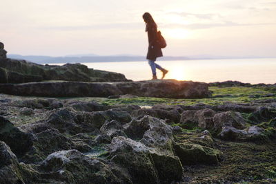 Woman standing on rock by sea against sky