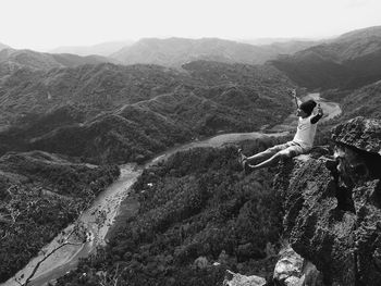 Young man with arms outstretched sitting on cliff
