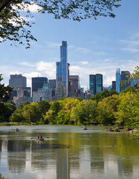 Scenic view of lake and trees against sky in city on sunny day at central park