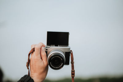 Close-up of man holding camera against sky