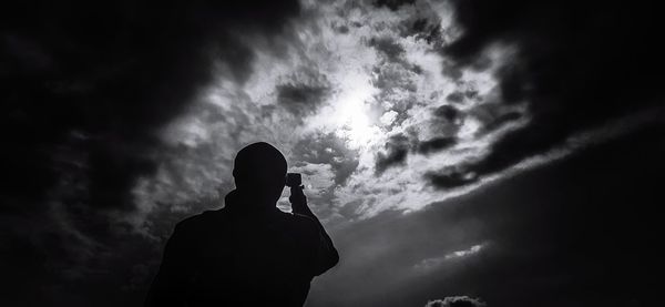 Low angle view of silhouette man photographing against sky