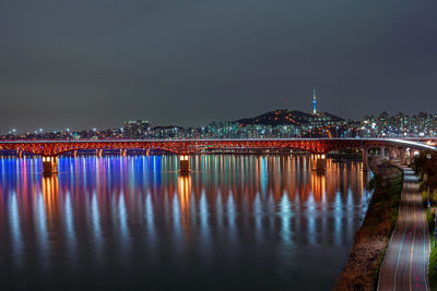 Illuminated bridge over river in city at night