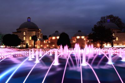 Illuminated fountain amidst buildings in city at night