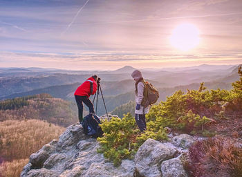 Hiker and photographer stay with tripod on cliff and takes photos. two people stay at tripod on peak