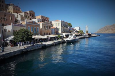 Buildings by sea against clear blue sky