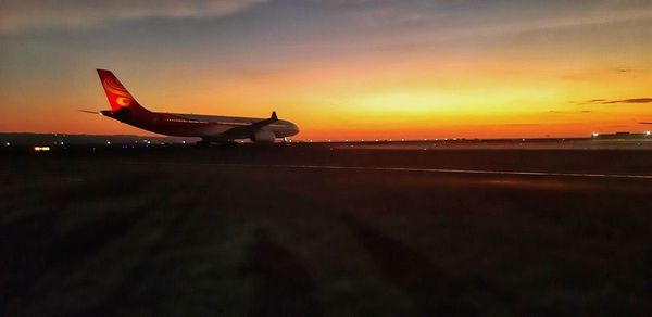 Airplane at airport runway against sky during sunset