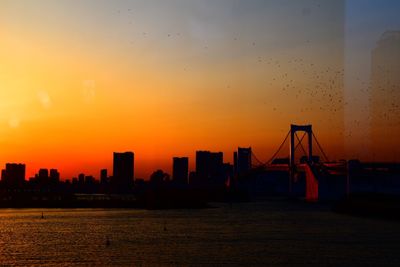 Silhouette buildings by sea against sky during sunset