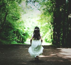 Rear view of girl in white dress walking at forest