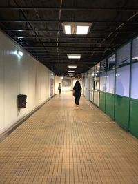 Rear view of person walking in illuminated passage 