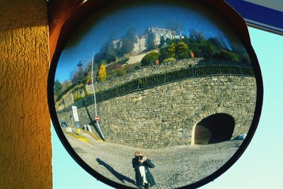 Reflection of man in glass mirror against sky