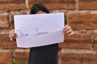 Woman holding text on paper against brick wall