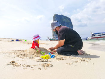 Father buried daughter at beach against sky