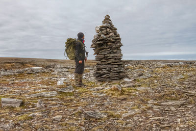 Man looking at stacked stones standing on land against sky
