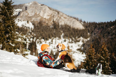 Rear view of woman sitting on snow with her dog