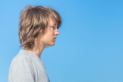 Boy looking away by against clear blue sky