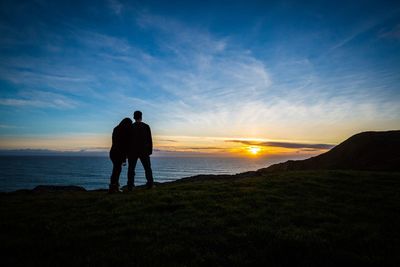 Silhouette couple looking at sea against sky during sunset