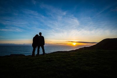 Rear view of silhouette man standing on shore against sky during sunset