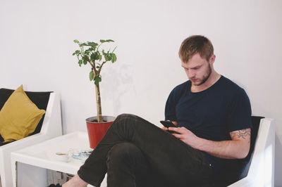 Young businessman using smart phone while sitting at lobby in creative office