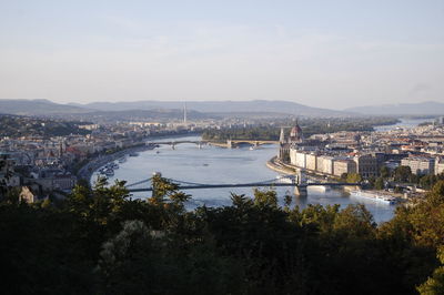 Bridge over river by cityscape against sky