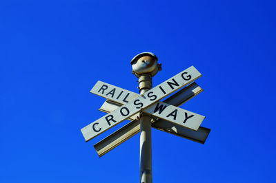 Low angle view of railroad crossing signal against clear blue sky