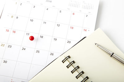 Close-up of diary with pen and thumbtack pinned calendar on table