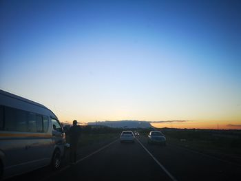 Cars on road against clear sky during sunset