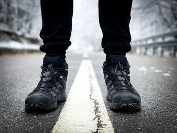 Man with black hiking boots in the middle of a road with trees covered in snow in the background