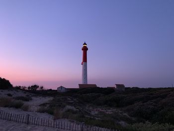Lighthouse amidst buildings against sky during sunset