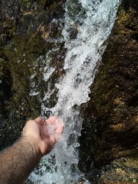 Cropped image of person hand by waterfall