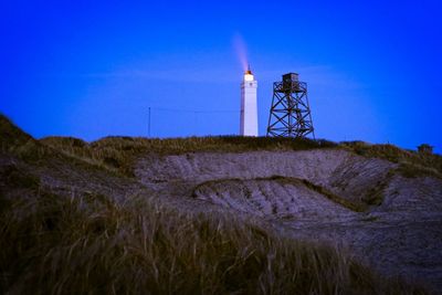 Lighthouse on field against clear blue sky