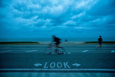 Blurred motion of man riding bicycle by sea on road