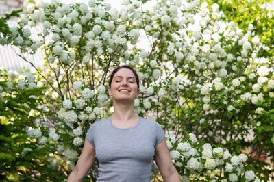 Smiling woman with eyes closed in front of flowering plant