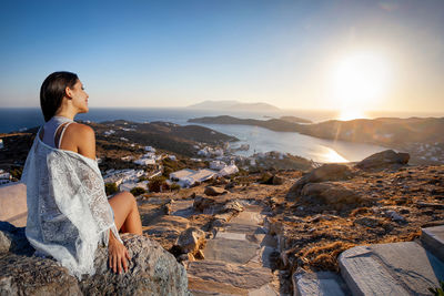 Smiling woman sitting on rock against sky