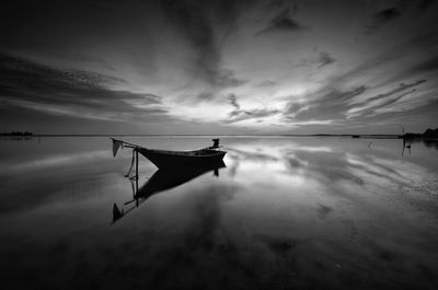 Fishing boat moored in sea against sky during sunset