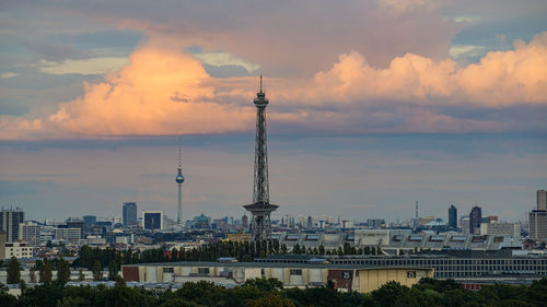 Communications tower in city against cloudy sky