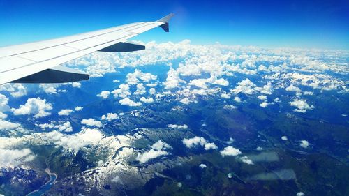 Aerial view of airplane wing over landscape against blue sky