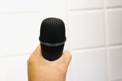 Close-up of hand holding microphone against wall