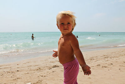 Full length of shirtless boy on beach against sky