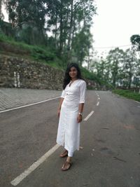 Full length portrait of young woman standing on road