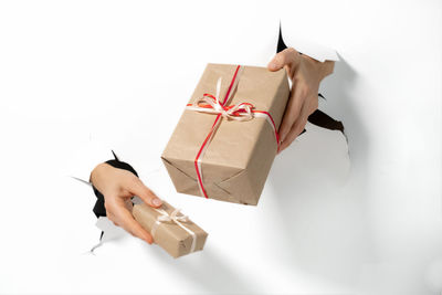 Close-up of female hand holding gift with ribbon through a torn white paper. creative present