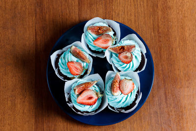 The plate of tasty cupcakes decorated with strawberry, fig and cream