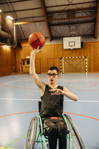 Girl with disability playing basketball while sitting on wheelchair at sports court