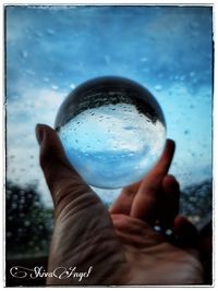 Close-up of hand holding glass against sky