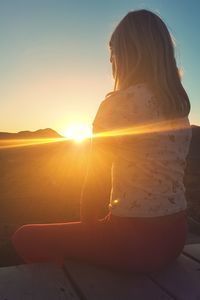 Rear view of woman sitting against sky during sunset