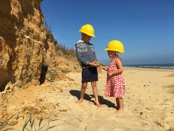 Siblings wearing hardhat while standing on beach