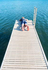 Young blond boy lying on pier over a lake watch fish in blue water below. boy enjoys his childhood.