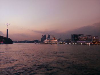 Illuminated buildings in city by river during sunset 